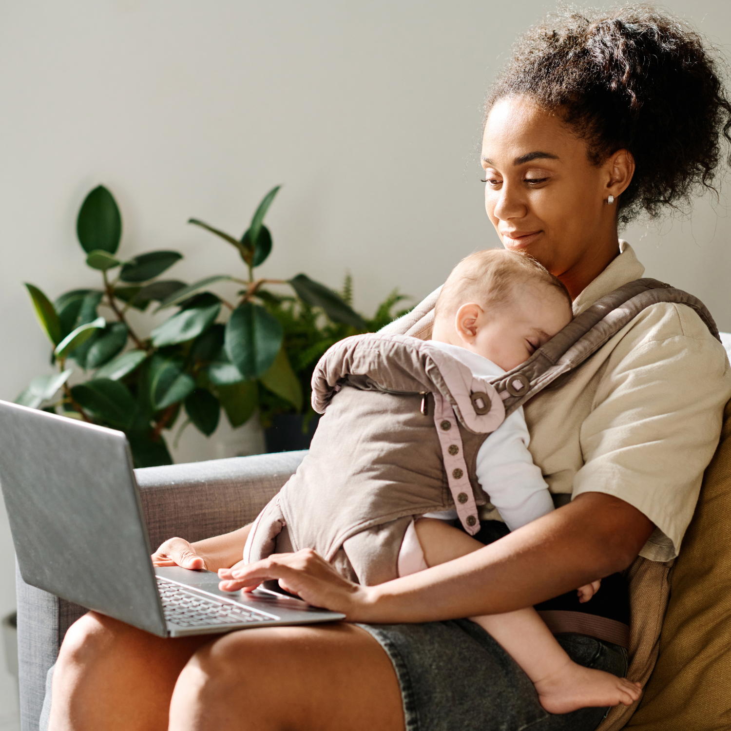 a mother carrying her baby on her lap while typing on a laptop